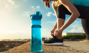 Female runner tying her shoe next to bottle of water.