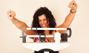 Woman celebrating weight loss on a medical weight scale.