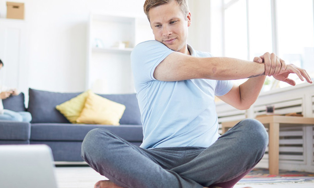 man stretching right arm while sitting on the floor