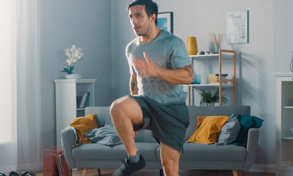 Man in T-shirt and Shorts is Energetically Jogging in Place at Home
